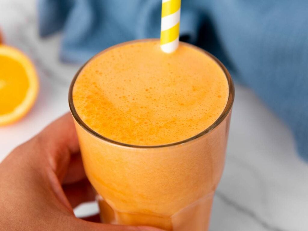 A glass of orange carrot juice with a yellow and white striped straw.