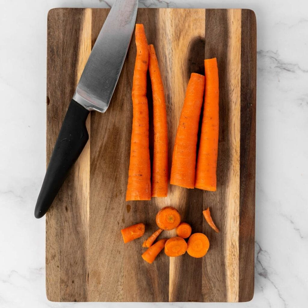 A knife and partially sliced carrots are placed on a wooden cutting board.