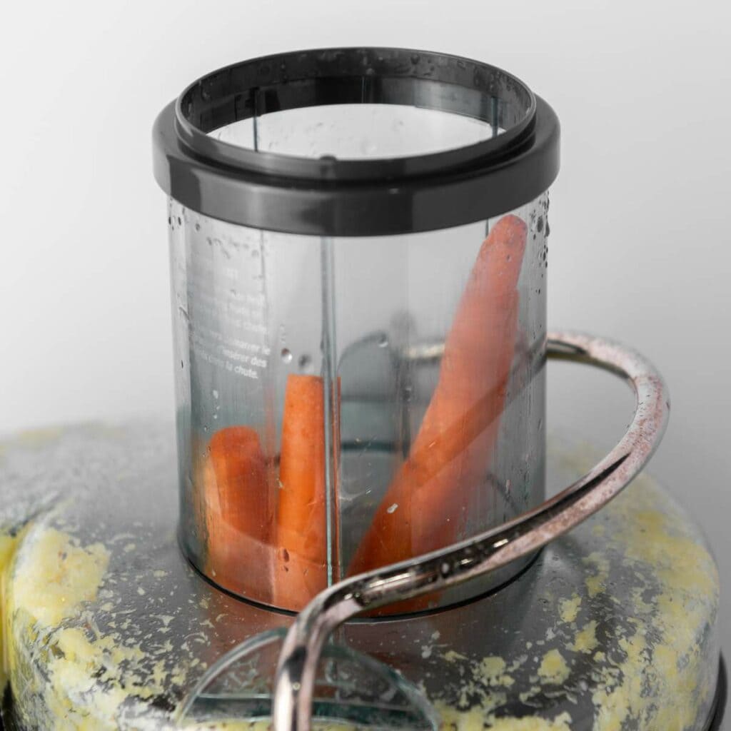 A transparent container with two whole carrots and water droplets.