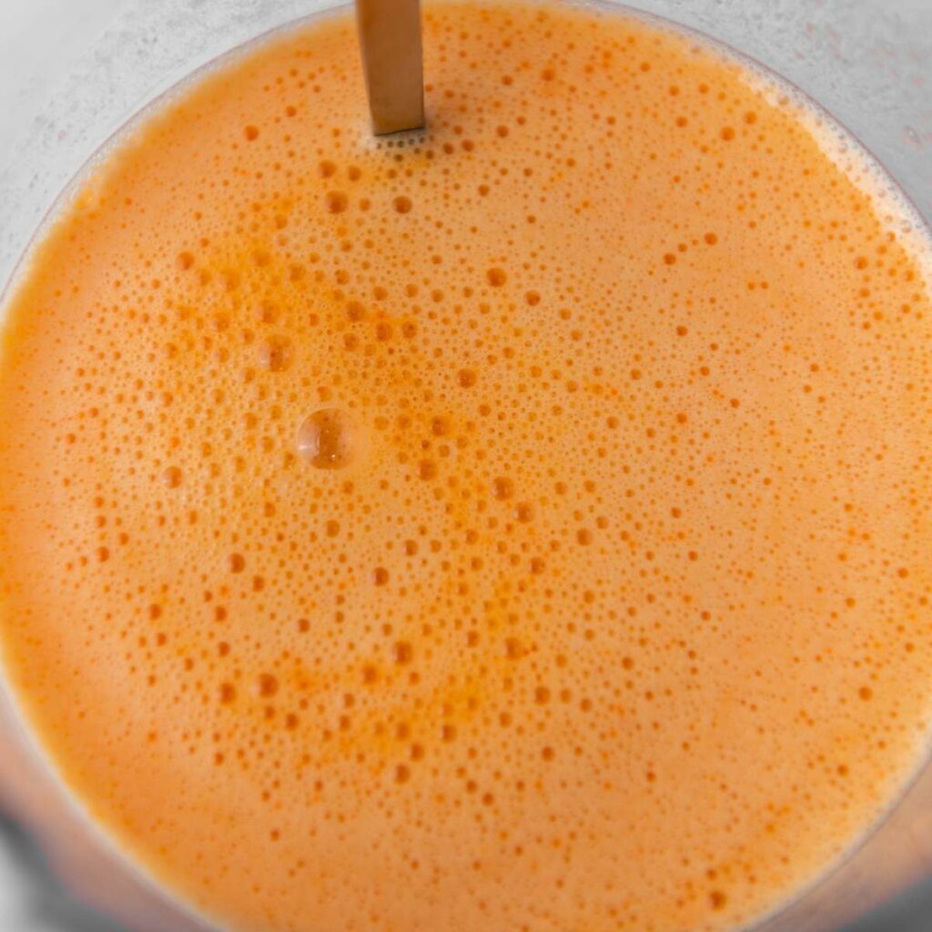 Close-up of orange foamy liquid in a blender.