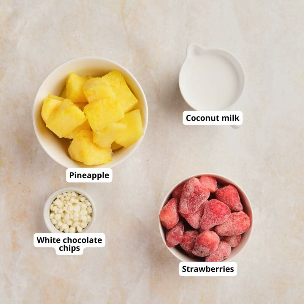 Four bowls of pineapple and strawberry smoothie ingredients are labeled and arranged on a light surface.