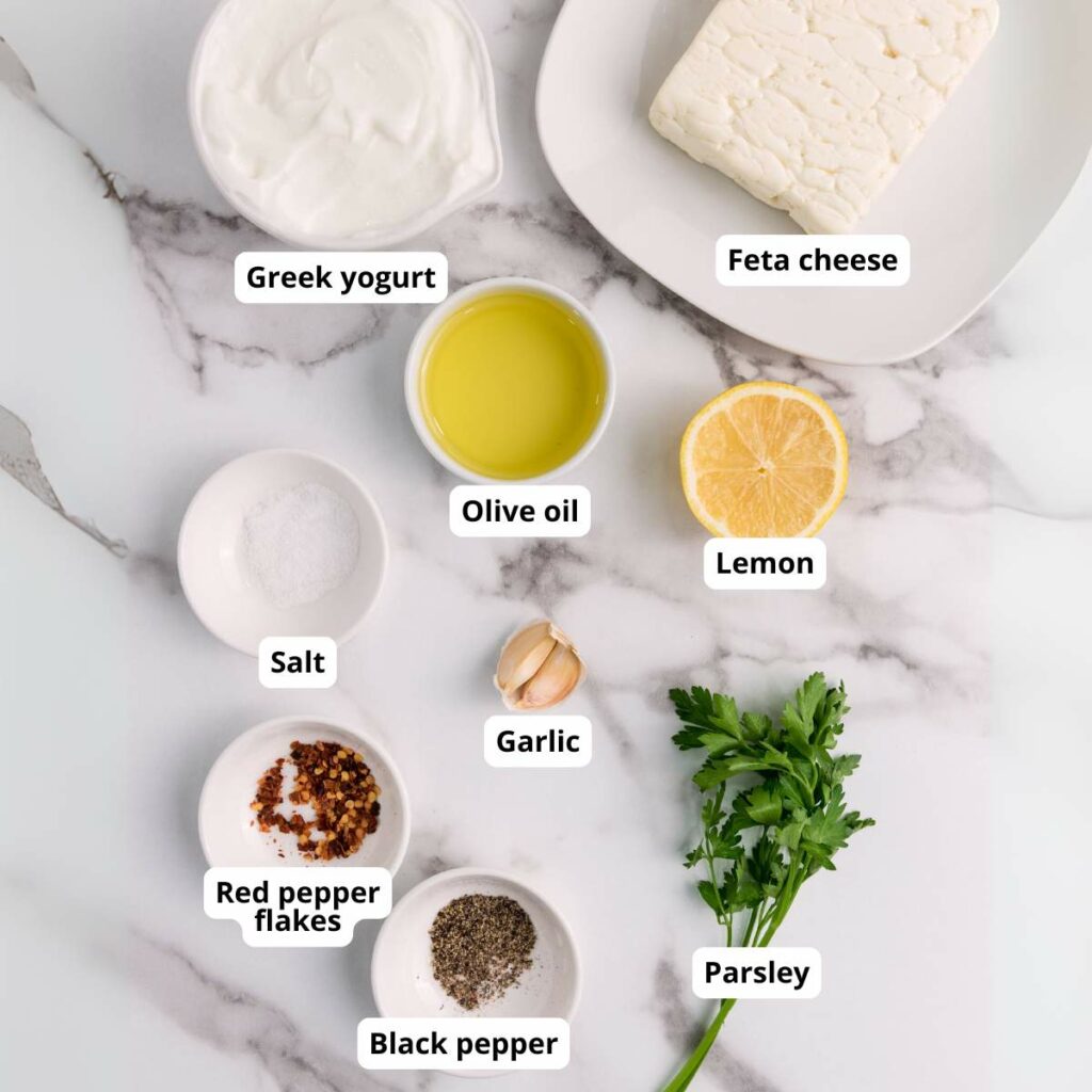 Ingredients for whipped feta cheese dip recipe arranged on a marble surface,.