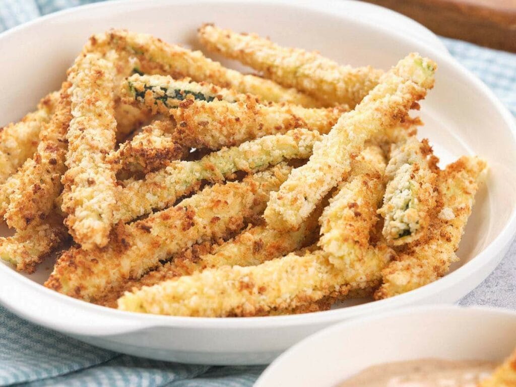 A white bowl filled with crispy, golden-brown breaded zucchini fries.