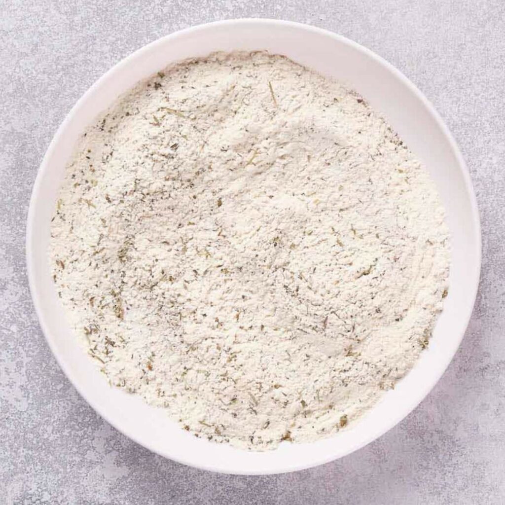 A white bowl filled with a mixture of flour and dried herbs.