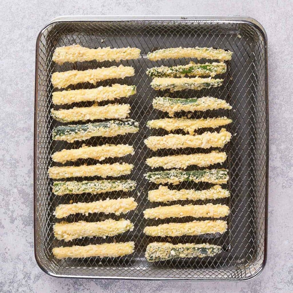 Breaded zucchini sticks arranged in rows on a wire rack.