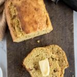 Half a loaf of banana bread with a single slice next to it, on a wooden cutting board.