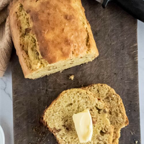 Half a loaf of banana bread with a single slice next to it, on a wooden cutting board.
