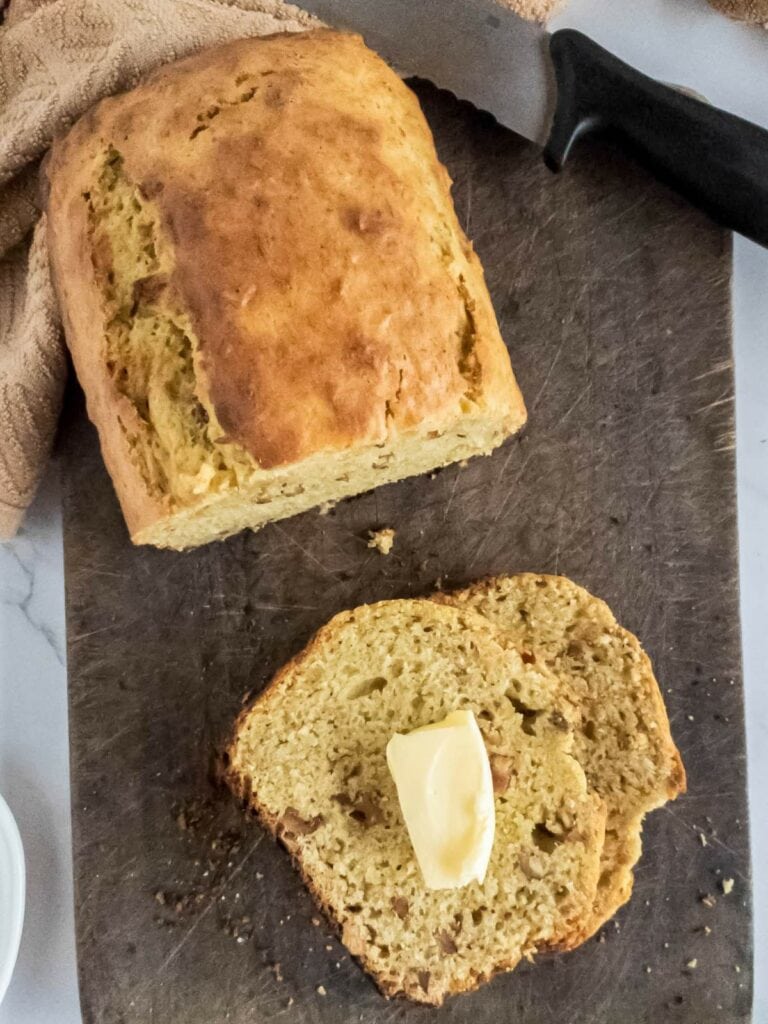 Half a loaf of banana bread with a single slice next to it, on a wooden cutting board.