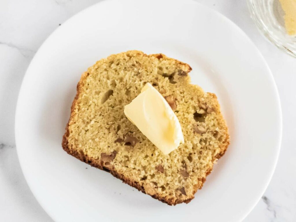 One slice of banana bread served on a white place with butter on top.
