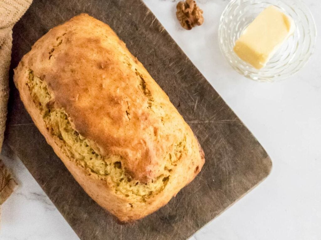 A loaf of banana bread on a wooden board with a stick of butter next to it.