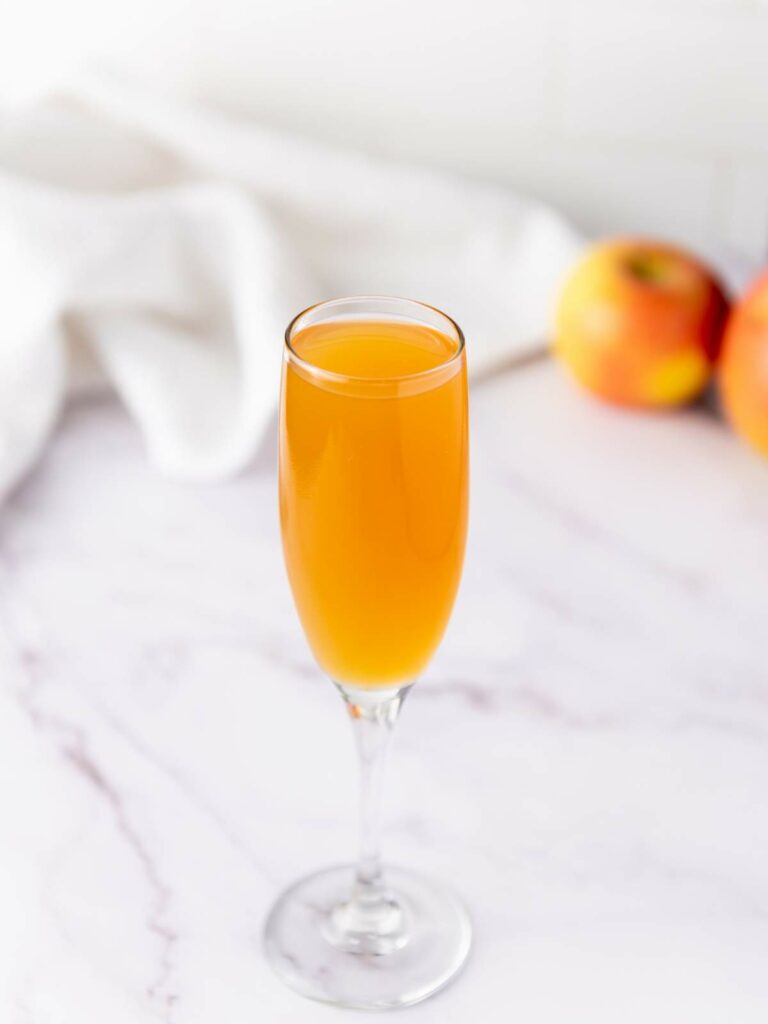 A glass of orange-colored drink in a champagne flute sits on a white marble surface.