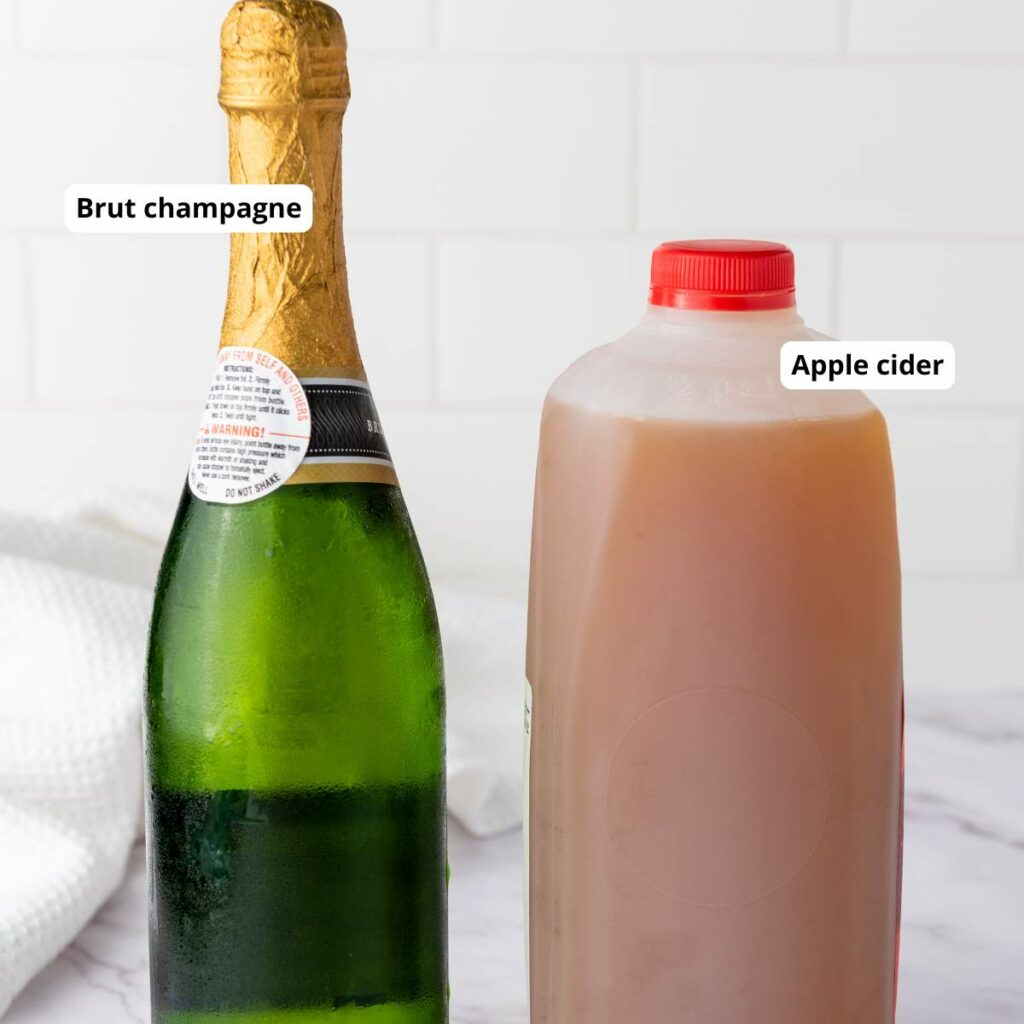 A bottle of brut champagne and a plastic jug of apple cider are placed side by side on a white counter.
