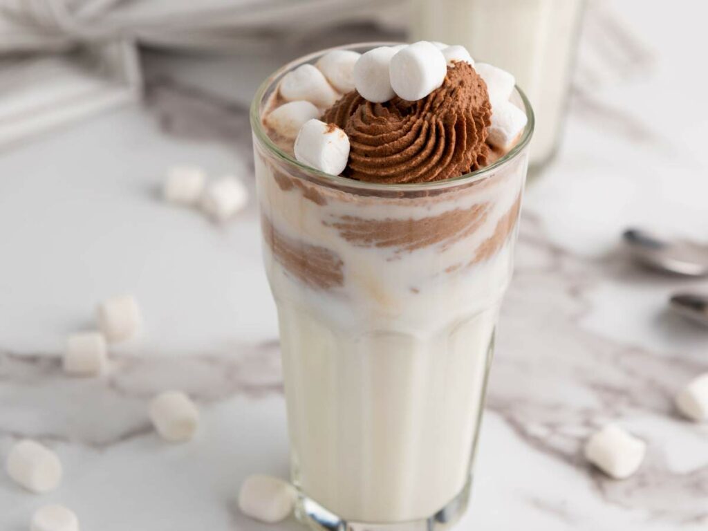 A glass of milk topped with chocolate whipped cream garnished with mini marshmallows.