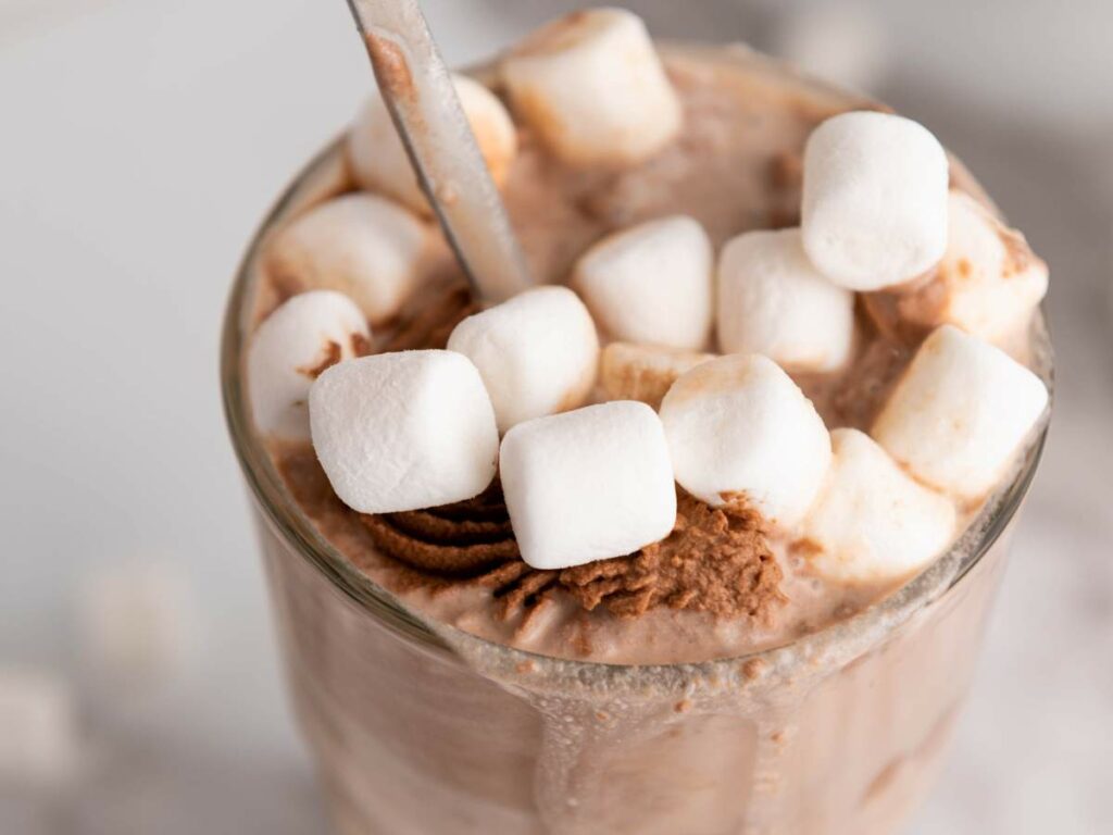 Close-up of chocolate-flavored milk with marshmallows and spoon inside.