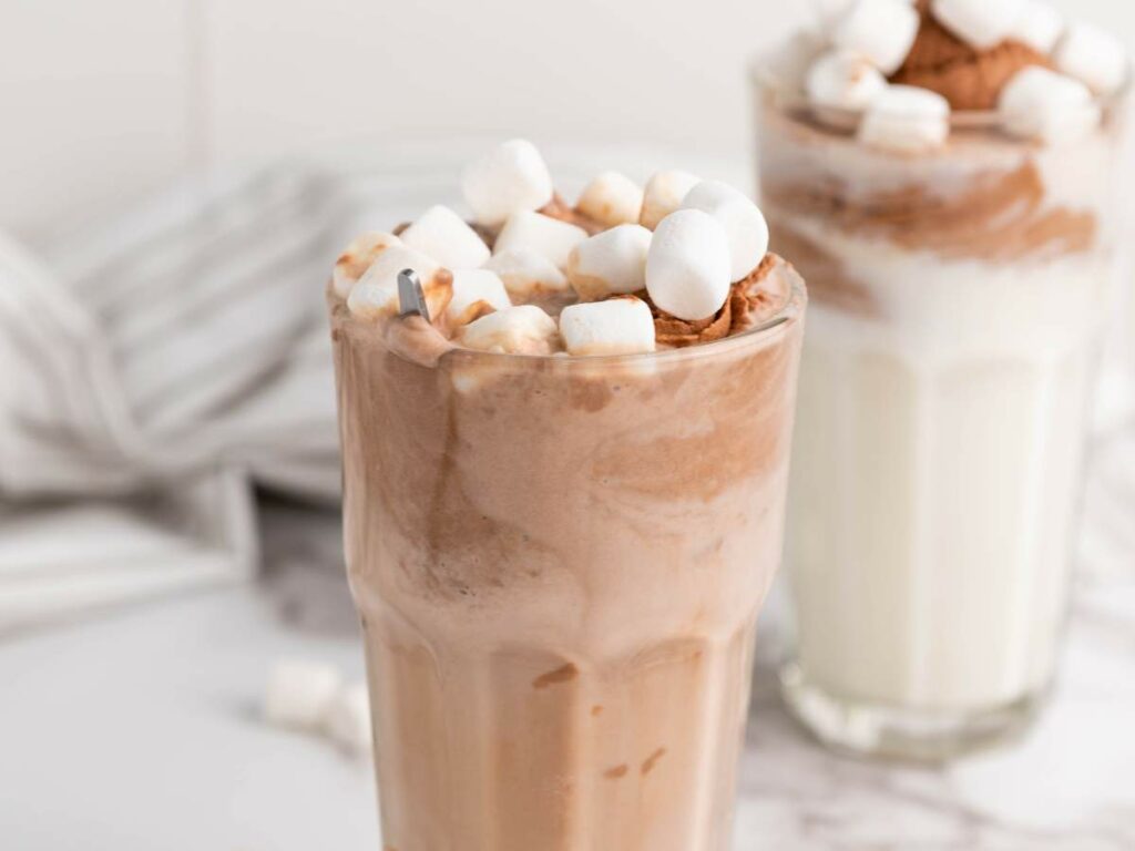 Two glasses of a delicious milk shake served in a tall glass and a generous topping of mini marshmallows.