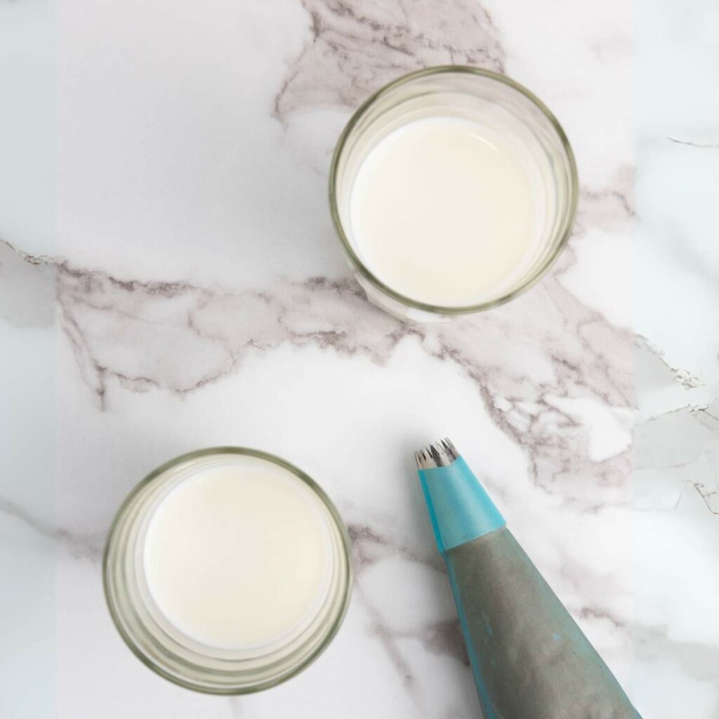 Two glasses of milk and a blue piping bag on a marble surface.