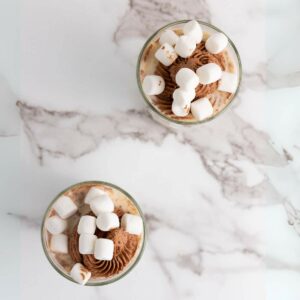 Two glasses of chocolate milk with whipped cream and marshmallows.