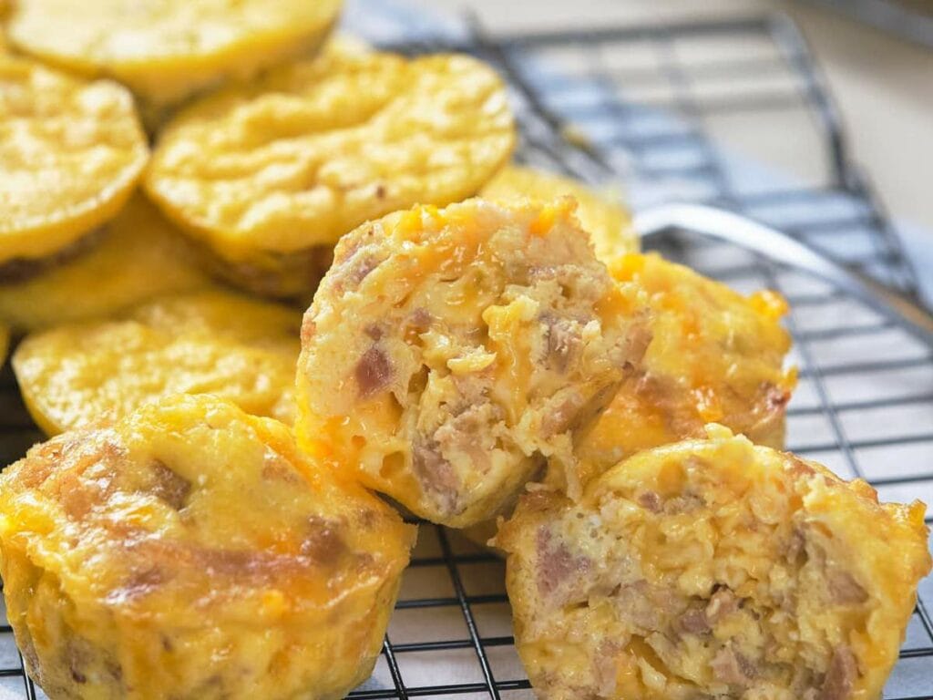 Rows of baked muffins, some with visible meat toppings, are cooling on a black wire rack.
