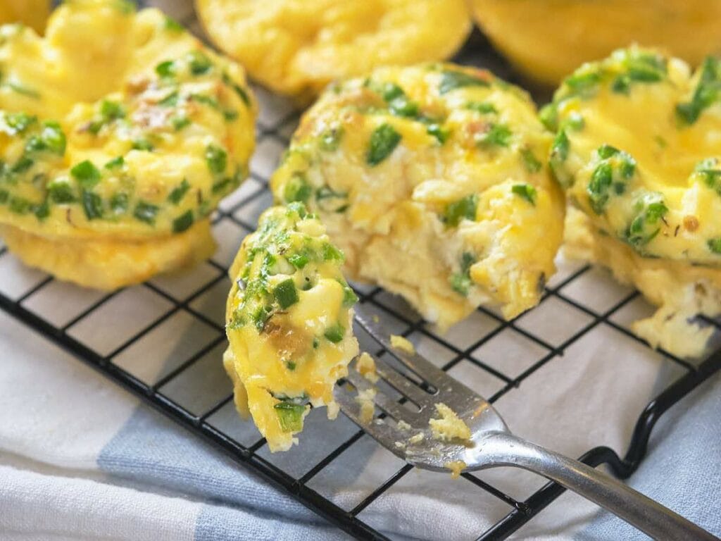 Freshly baked egg muffins with golden tops and green herb specks rest on a cooling rack.