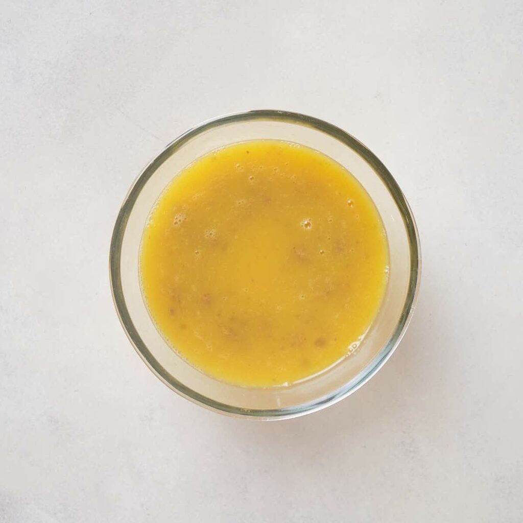 A glass bowl filled with whisked eggs and seasoning on a white surface.