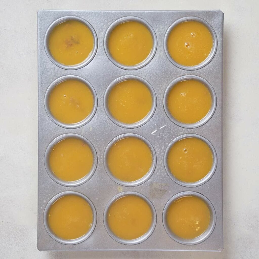 Muffin tin filled with plain egg mixture before adding mix-ins on a white surface.