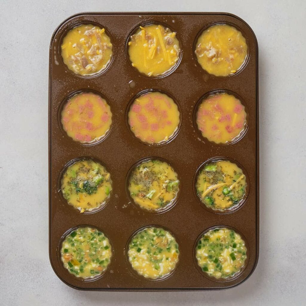Muffin tin with assorted egg bite flavors, each cup packed with colorful mix-ins.