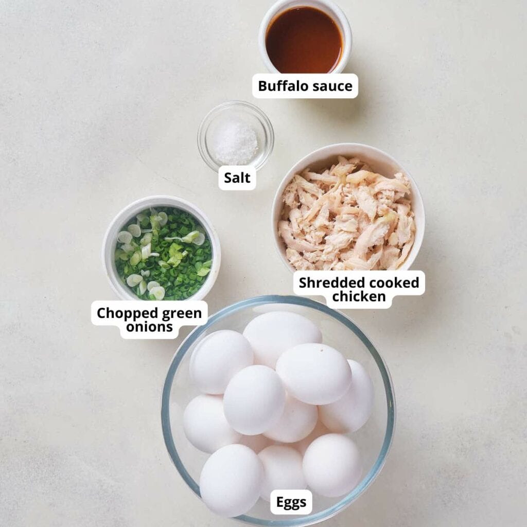 Ingredients labeled for buffalo chicken egg bites with eggs, arrange on a light surface.