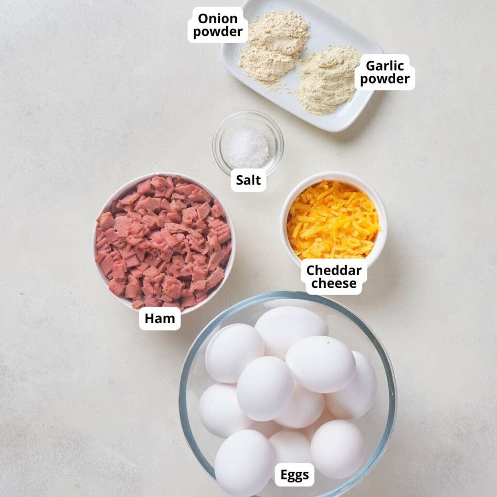 Ingredients for ham and cheese egg bites, all labeled on a white surface.