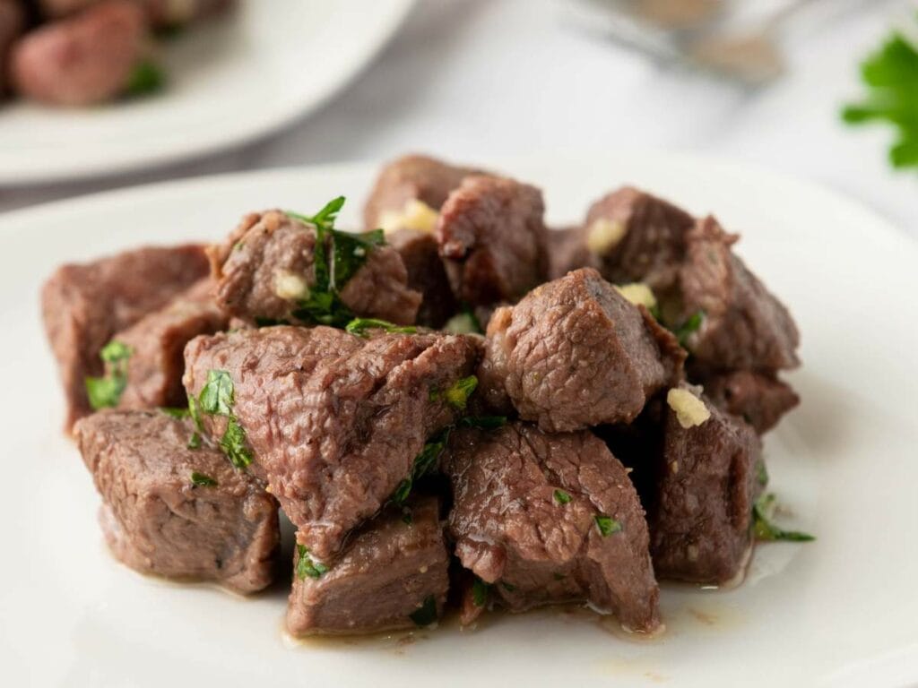 A close-up of tender beef garnished with fresh herbs on a white plate.