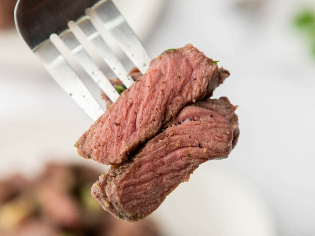 A fork holding two pieces of perfectly cooked steak, showing a juicy and tender interior.