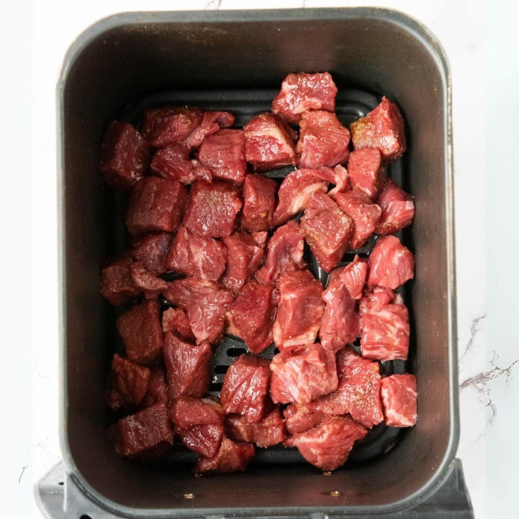Marinated steak bites are arranged in a single layer inside an air fryer basket.