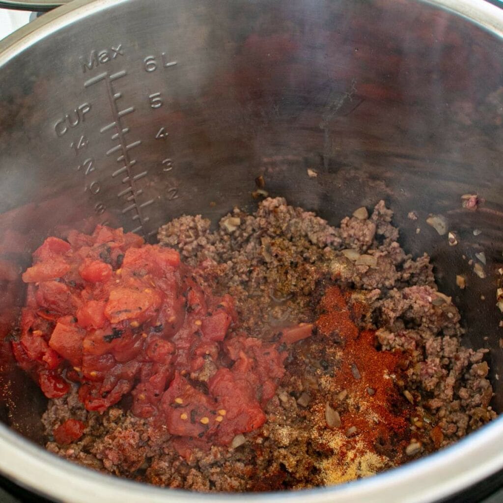 Ground beef, chopped onions, diced tomatoes, and spices cooking in the instant pot.