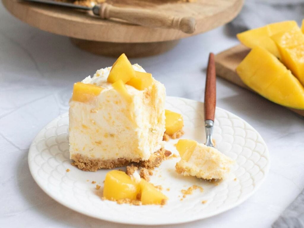 A slice of cake topped with mango pieces on a white plate, with a fork.