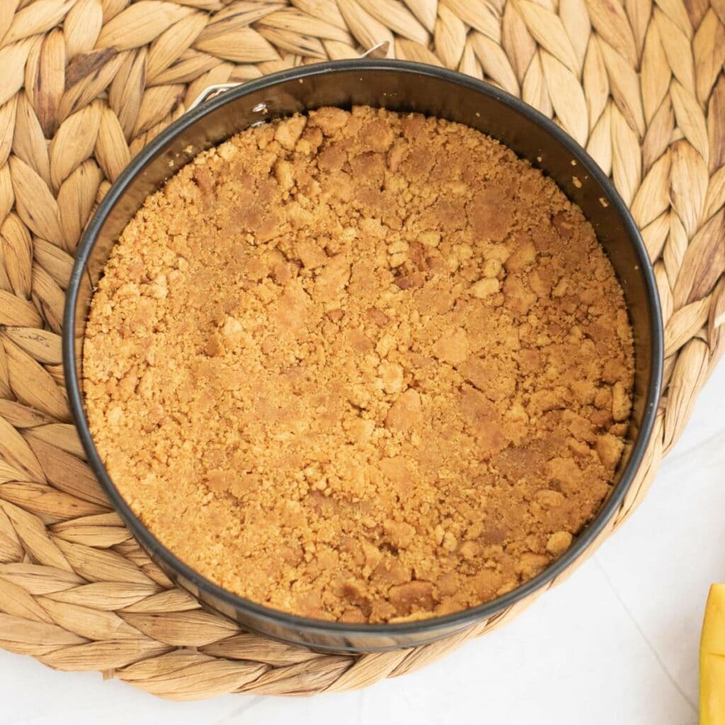 A round baking tin filled with a pressed graham cracker, placed on a woven mat.