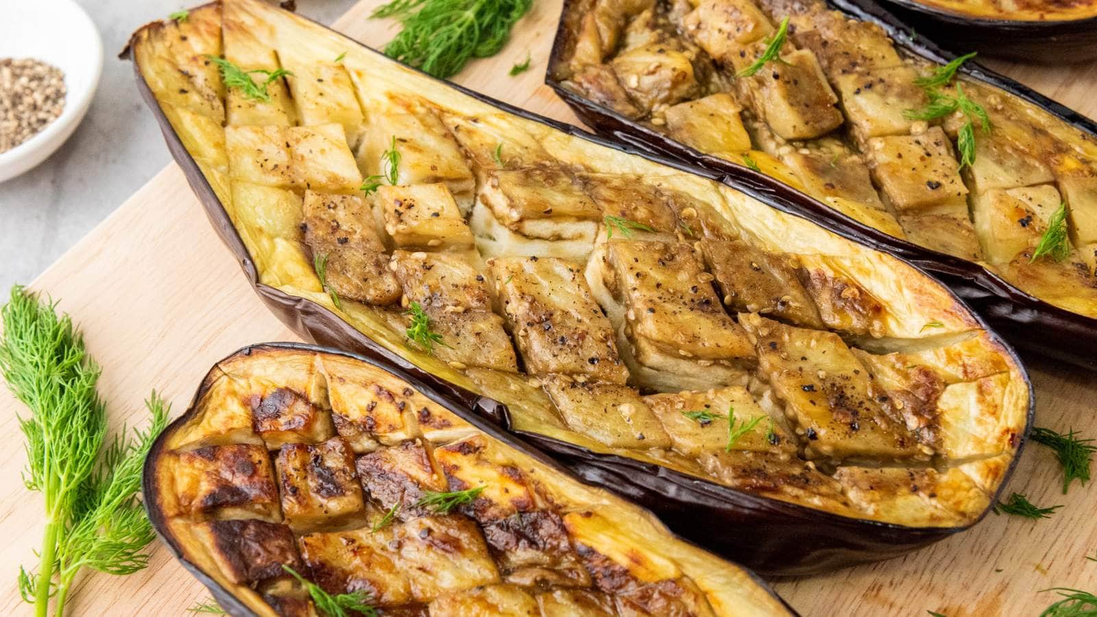 Halved baked eggplants with a scored, golden-brown surface, seasoned with herbs and pepper.