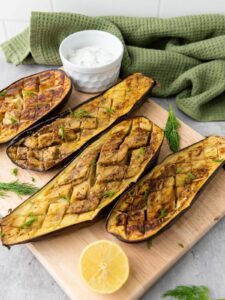 Four cooked eggplant halves with a crisscross pattern on a wooden board.