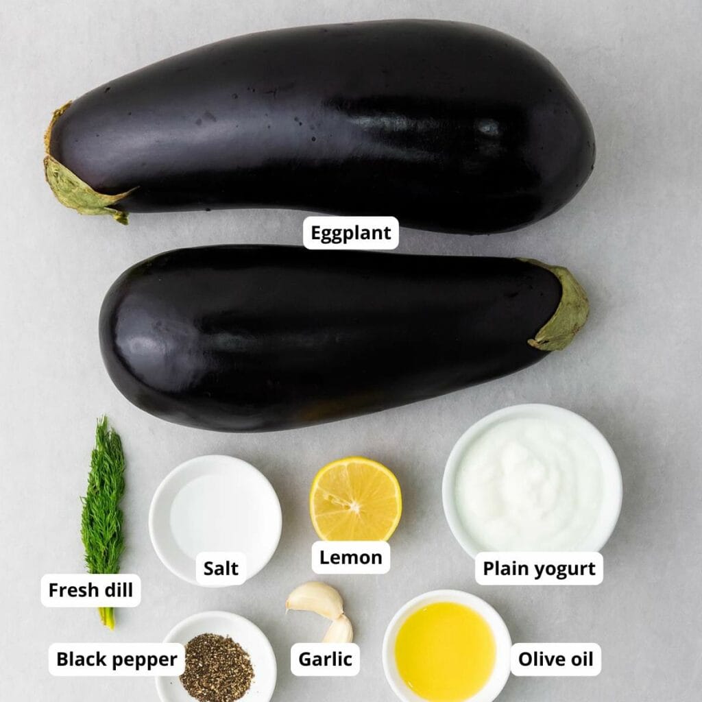 Baked eggplant ingredients are arranged on a white surface, each labeled accordingly.