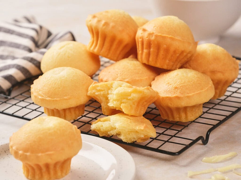 A group of muffins sits on a cooling rack, with one muffin broken in half showing its soft interior.