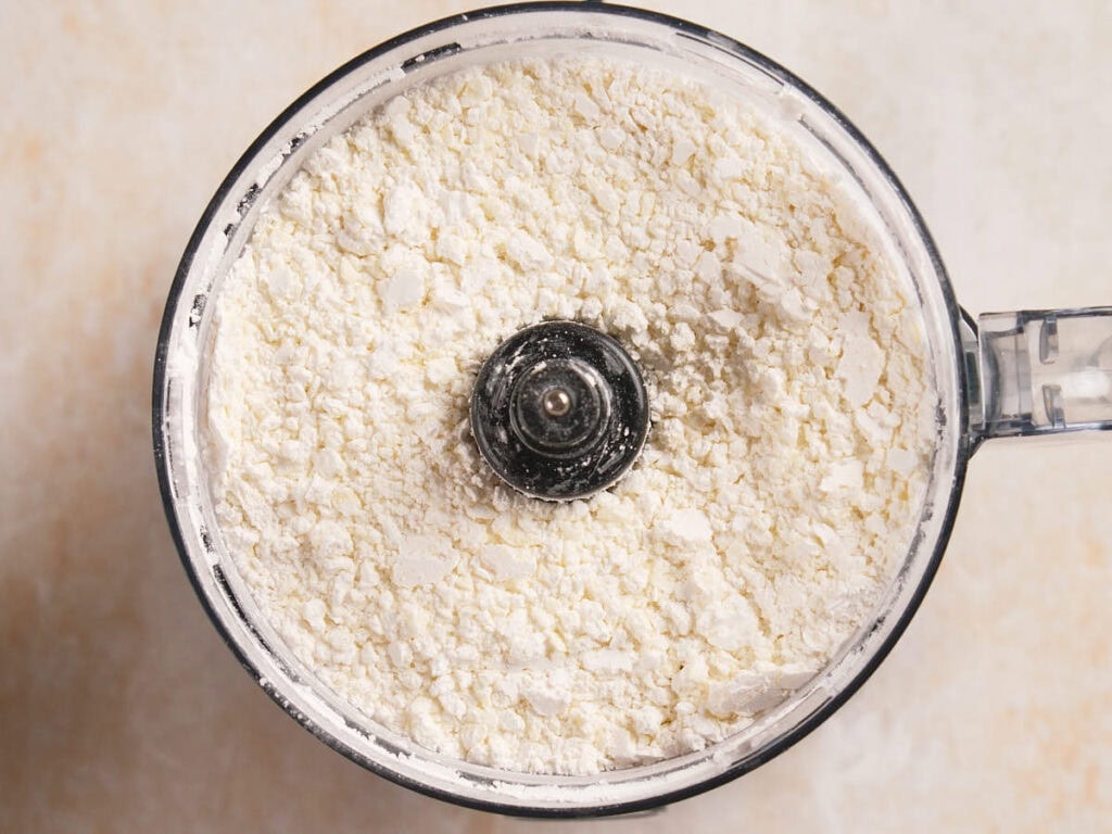 A food processor bowl filled with finely processed flour mixture, viewed from above.
