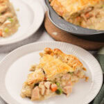 A slice of baked pie filled with chicken and vegetables on a white plate.