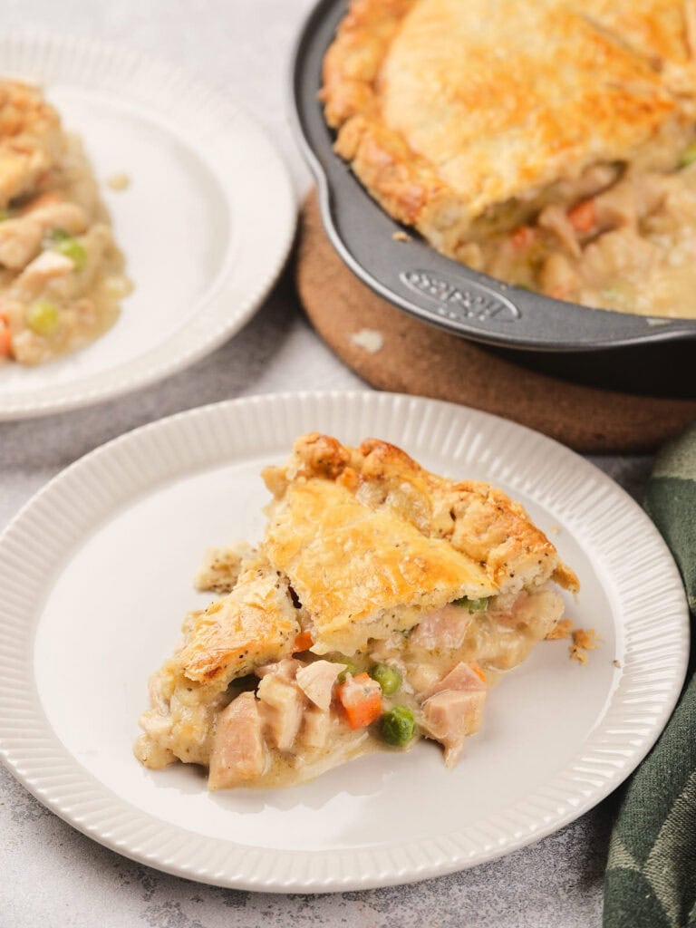 A slice of baked pie filled with chicken and vegetables on a white plate.