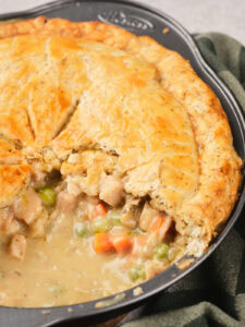 A close-up of a baked chicken pie in a pan with a golden crust, partially sliced to show the creamy filling.