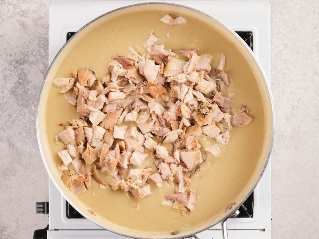 Chopped cooked chicken pieces in a creamy sauce simmering in a large skillet on a stovetop.