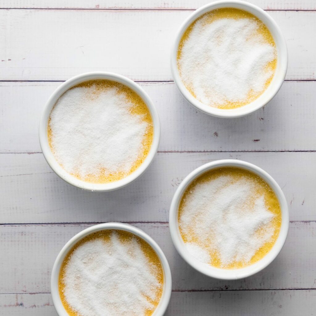 Four white ramekins filled with a yellow custard base topped with a layer of granulated sugar.