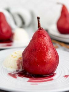 A poached pear in red wine sauce served on a white plate with a scoop of vanilla ice cream.