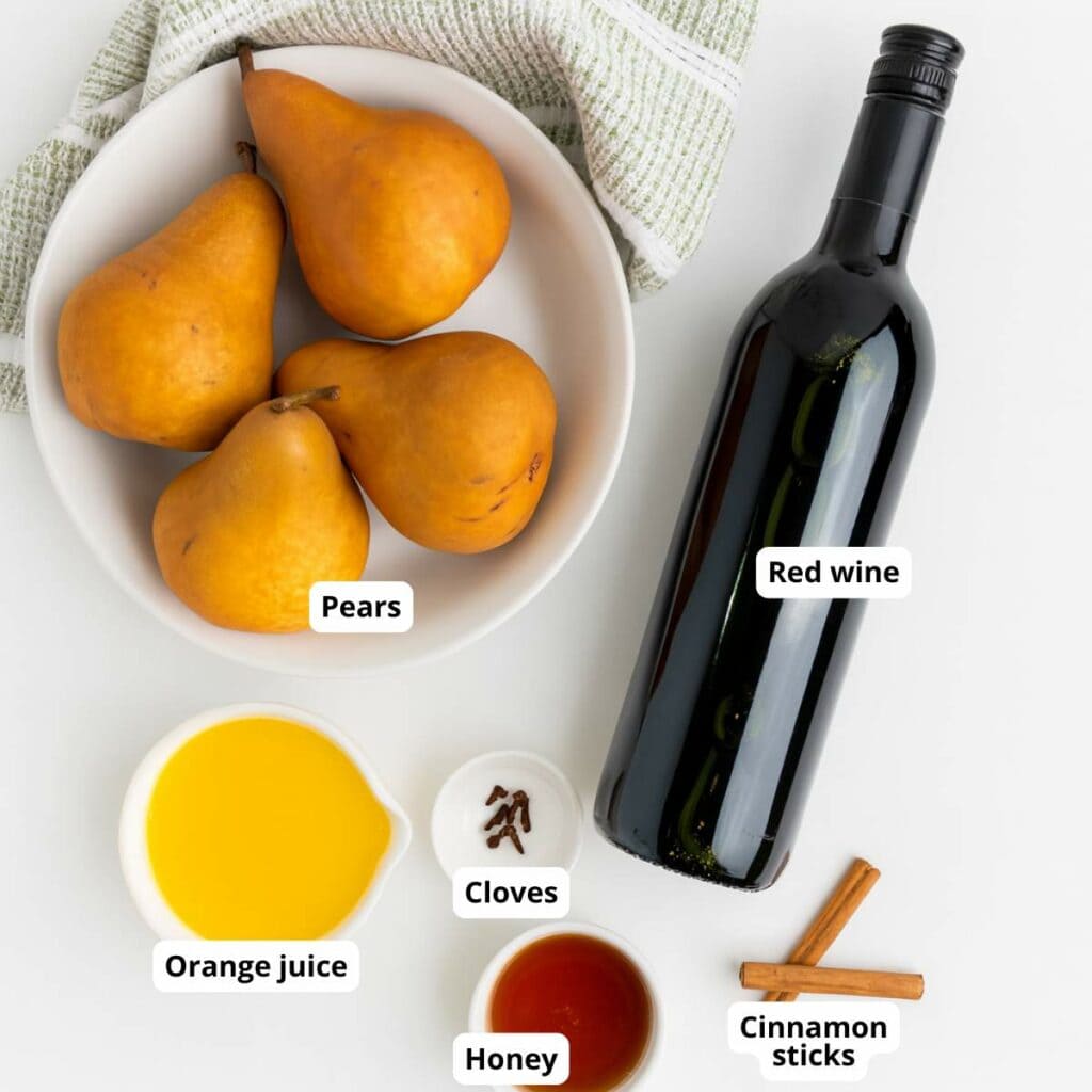 Labeled ingredients for poached pears recipe are arranged on a white surface.
