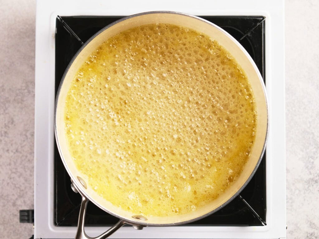 A saucepan filled with bubbling yellow liquid sits on a stove burner, viewed from above.