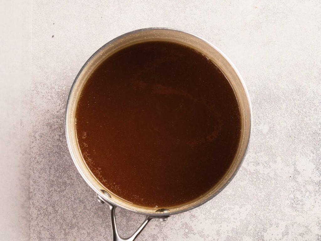 A metal saucepan filled with brown liquid, viewed from above, placed on a light textured surface.