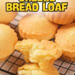 Several golden brown cheese bread loaves are cooling on a wire rack, with one loaf broken open to show interior.