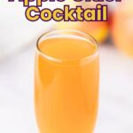 A clear glass filled with orange apple cider cocktail sits on a white surface.